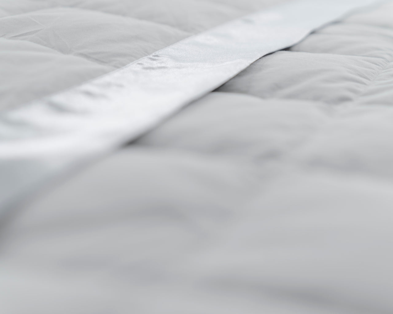 Close-up of a silver feather and down blanket showing the satin border and box quilting